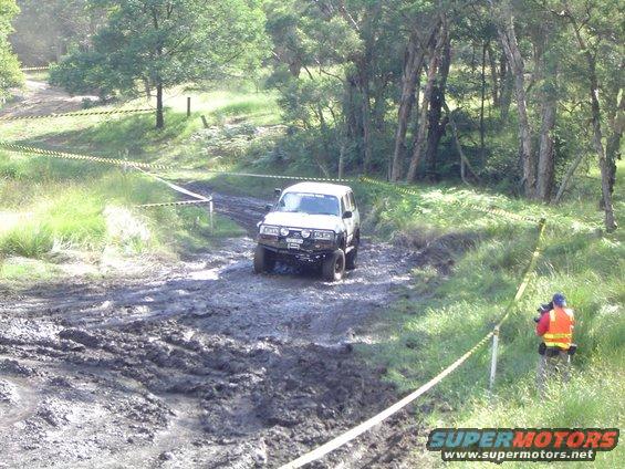White SUV with off-road tires and a bull bar navigating a muddy track