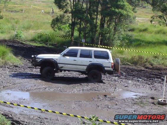 White SUV with spare tire on back stuck in mud on an off-road course