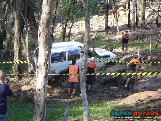 White SUV stuck in rocks, with yellow caution tape and people observing