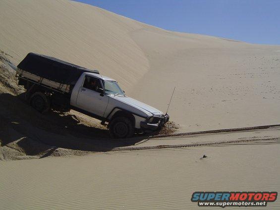 White pickup truck with black canopy driving on sand dune, front wheels turned