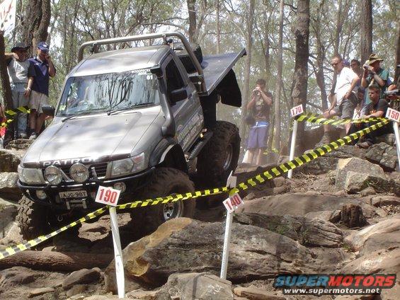 Silver Nissan Patrol off-roading vehicle with large tires and roll cage, navigating rocky terrain