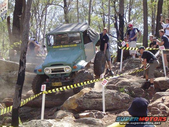 Green Toyota Land Cruiser FJ40 climbing a rocky hill with spectators watching. License plate GR1 642