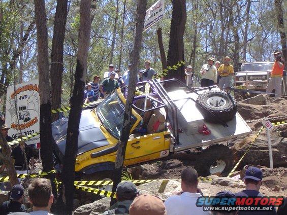 Yellow off-road vehicle with roll cage and spare tire on a rocky course