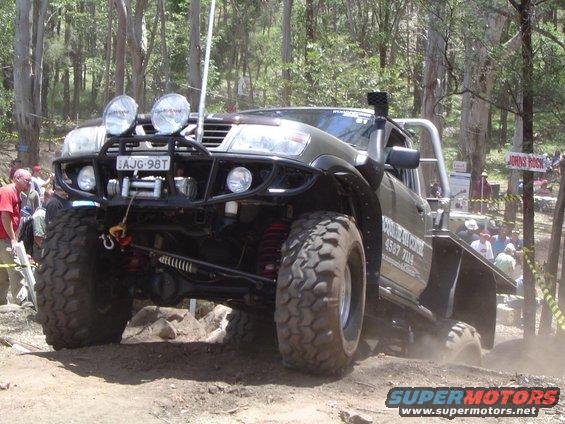 Olive green off-road vehicle with large tires and winch, angled on a dirt track