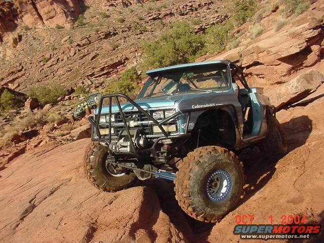 Light blue off-road truck with roll cage and large tires climbing a rocky incline