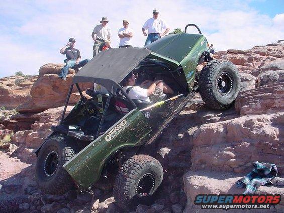 Green off-road vehicle climbing rocks, driver visible inside
