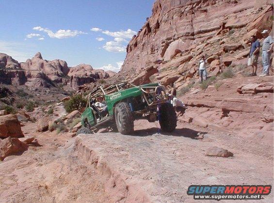 Green off-road buggy with roll cage climbing a steep, rocky trail