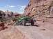 1988 Ford Bronco - A modified green off-road buggy navigates a challenging rocky terrain under a bright blue sky.