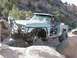 1988 Ford Bronco - Modified pickup truck with large tires and roll cage driving over rocks off-road.