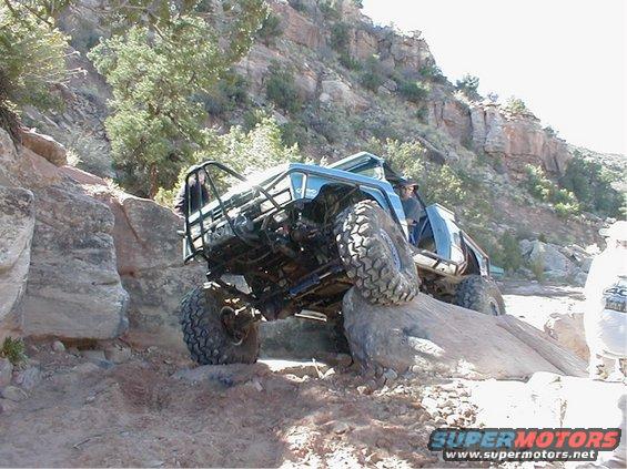 Off-road vehicle with roll cage climbing over a large rock on a trail