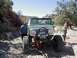 1988 Ford Bronco - A modified green SUV with oversized tires and a winch is parked on a rocky trail with two people standing nearby.