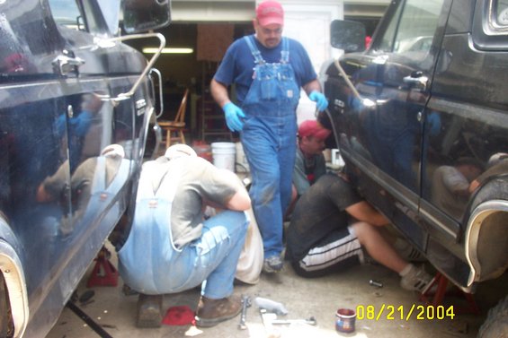 Two dark pickup trucks on jacks, men working underneath them