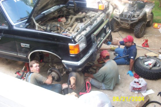 Black truck with hood open, men working on front suspension. ATV in background
