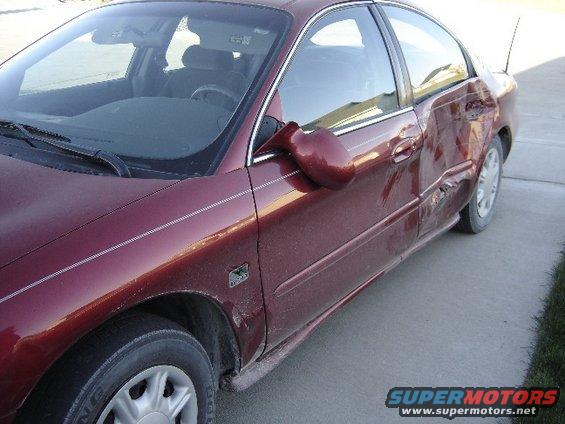 maroon sedan, likely from the early 2000s, parked on a concrete driveway with heavy damage to the rear passenger door and quarter panel