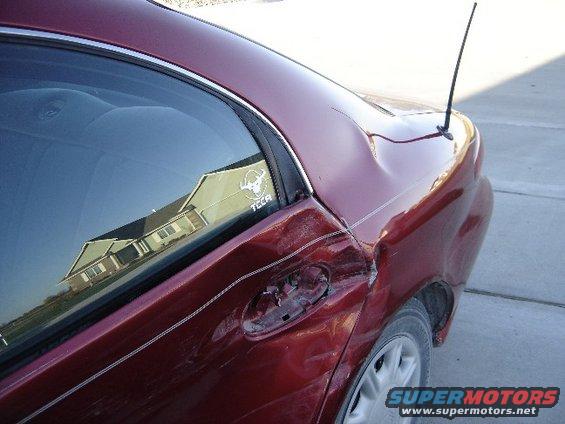 Red sedan rear quarter panel with significant damage and a skull sticker on the window