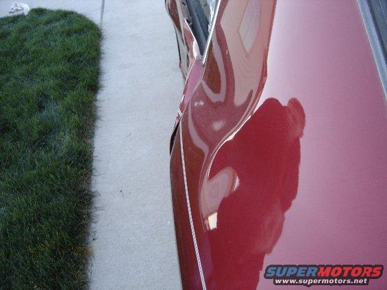 damaged red car door, shows reflection of sky and a person