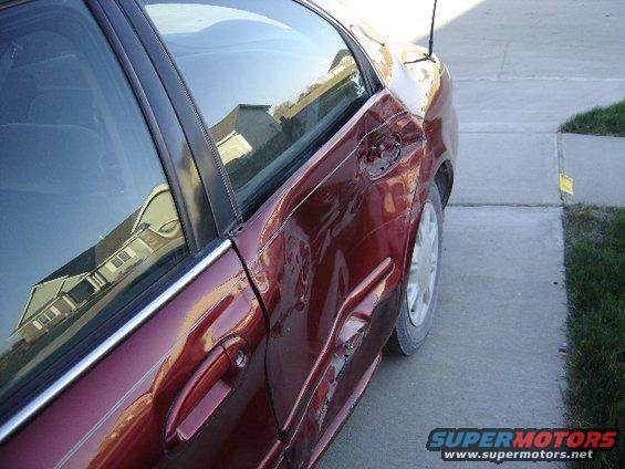 side view of a red sedan with significant damage to the rear passenger door and quarter panel