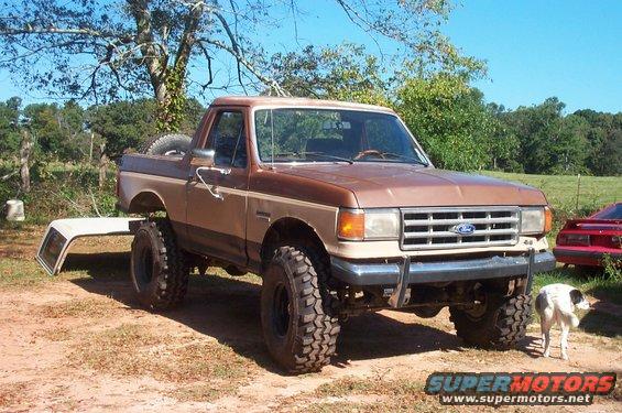 1987 Ford Bronco lifted with large tires, removable top off and leaning against the side
