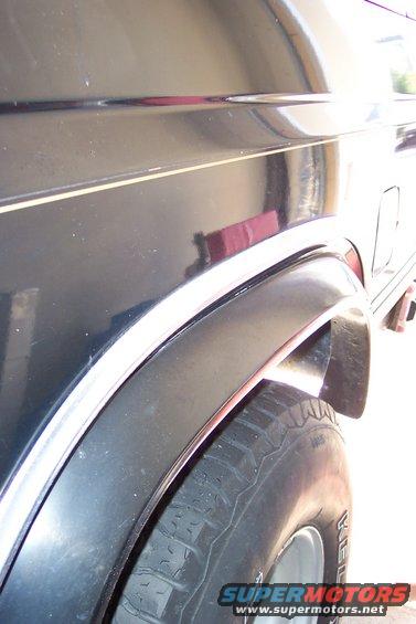 Close-up of a dark SUV's rear fender and tire, showing a chrome trim line