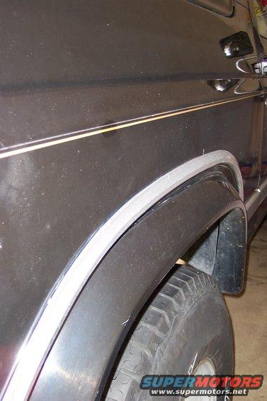 Dark SUV rear quarter panel with a chrome trim line above the fender flare and a tire. The body style suggests an 80s model