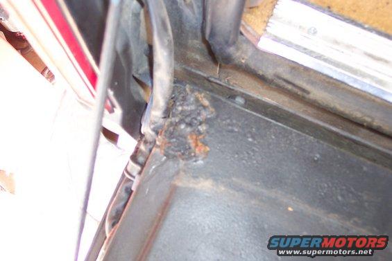 Close-up of rust and corrosion on a dark gray vehicle body panel, with some red trim visible on the left