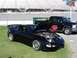 1995 Ford Taurus - A black sports car and a black pickup truck are parked on grass with stadium bleachers in the background.