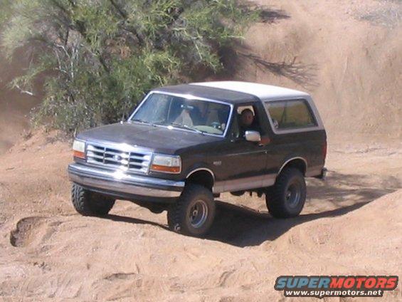 Black Ford Bronco with white top driving on a dirt trail, kicking up dust