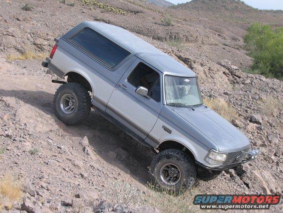 1995 Ford Bronco off-roading on a rocky hill, two-tone silver and gray