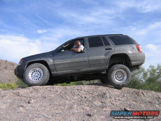Gray Jeep Grand Cherokee with aftermarket wheels driving on a dirt hill