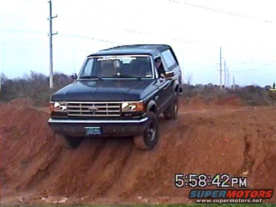 Dark blue Ford Bronco driving on a dirt mound, front 3/4 view