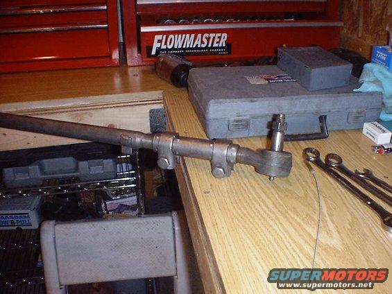 Steering linkage part with tie rod end, on a wooden surface next to tools