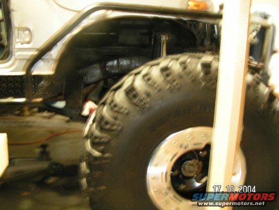 Close-up of a large off-road tire and wheel well of a vehicle, with a wooden post in the foreground