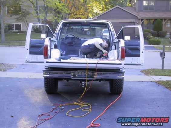 Guy working on the inside of a white Ford truck bed, doors open. Power cords run from the back