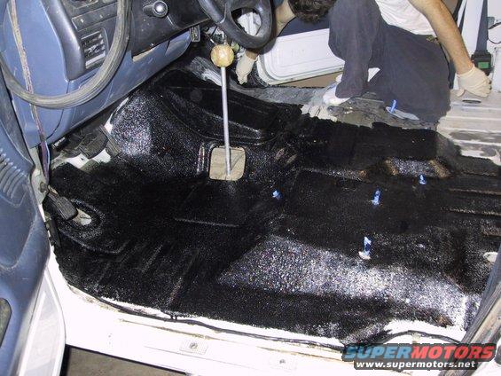 Vehicle interior floor being coated with black protective material, showing a manual transmission shifter