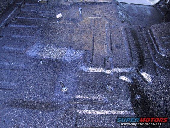 vehicle floor with spray-on bedliner, showing some bolts and a white tag
