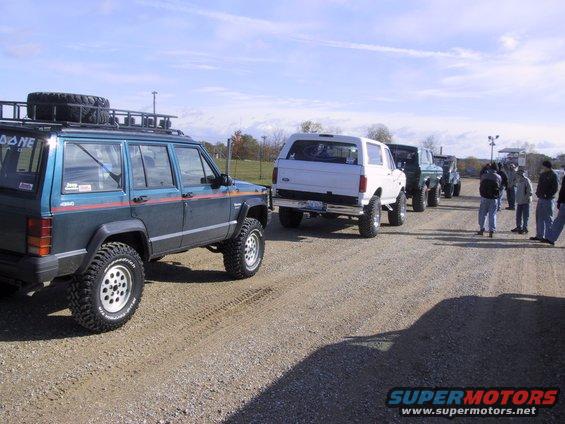White 1993 Ford Bronco rear view, parked on gravel with other vehicles and people