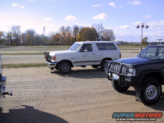 White 1993 Ford Bronco with aftermarket lights parked next to a dark SUV