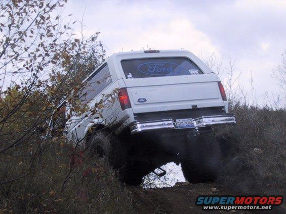 White 1993 Ford Bronco on a dirt incline, rear view, with large tires and a Ford logo on the rear window