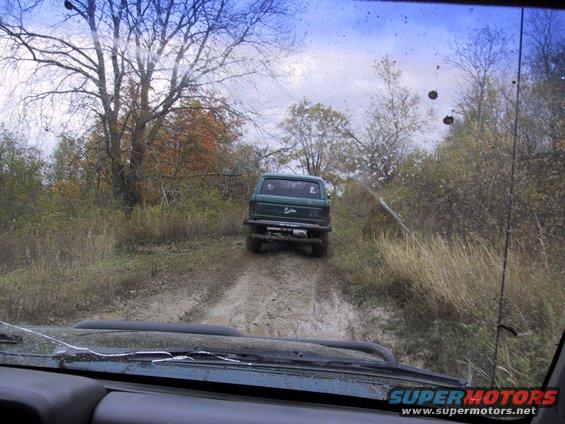 Green SUV driving on a muddy trail, seen from another vehicle's interior