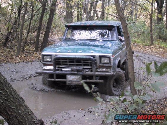 Green 1978 Ford Bronco driving through mud puddle