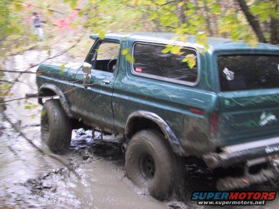 Green Ford Bronco with custom pinstriping driving through a muddy trail, front passenger side wheel deep in mud