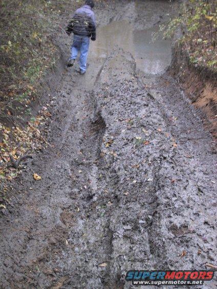 Muddy off-road trail with tire tracks and a person walking away