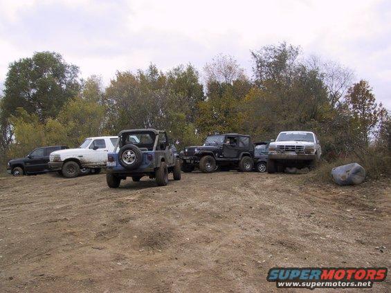 Several off-road vehicles parked on a dirt lot with trees in the background