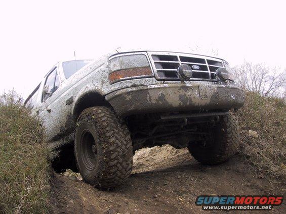 Mud-covered 1992 Ford Bronco driving off-road, front 3/4 view