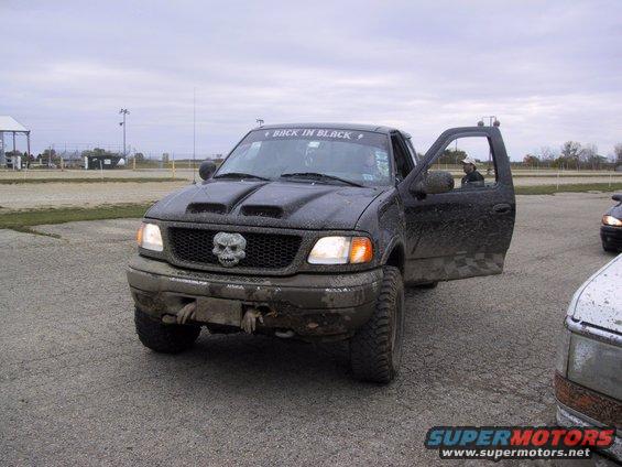 Black Ford F-150 truck, front view, driver's door open, skull grille emblem, mud-splattered