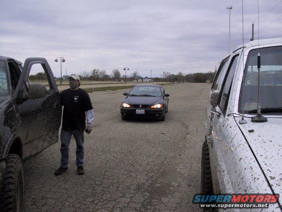 Man standing by a black SUV, a dark sedan in the middle, and a silver SUV on the right