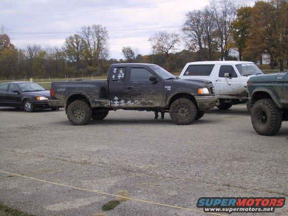 Black pickup truck with lifted suspension and off-road tires, parked next to a white SUV and a green vehicle