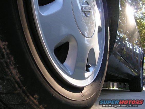 Close-up of a Nissan wheel and the side of a dark car. The sun is glinting off the car's body