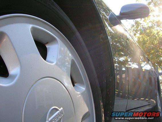 Silver Nissan wheel and dark-colored car fender with sun glare