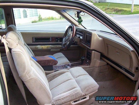 1989 Buick Riviera interior with tan velour seats, wood trim, and a green air freshener hanging from the rearview mirror